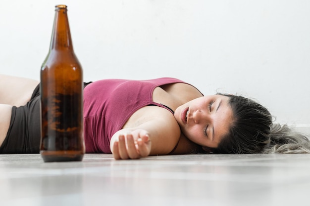 Zdjęcie pijana kobieta leżąca na podłodze, zemdlała w pobliżu butelki piwa.
