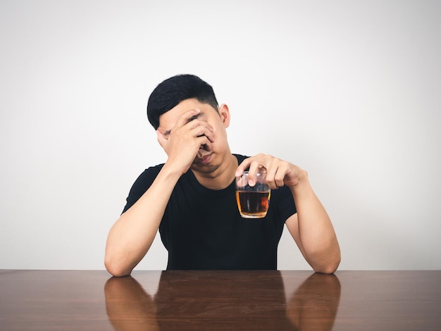 Pijany mężczyzna siedzi i trzyma szklankę alkoholu i zamyka twarz