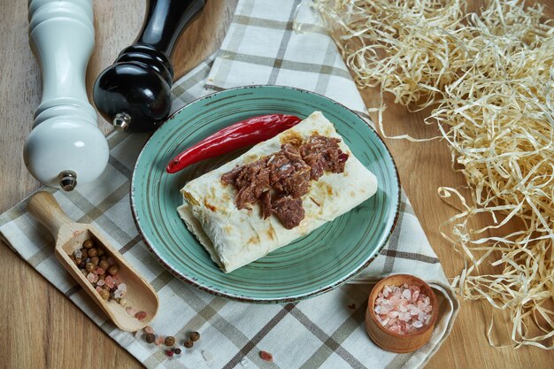 Zdjęcie pikantne burrito lub shawarma na niebieskim talerzu z tradycyjną gotowaną, miękką wołowiną w kompozycji z przyprawami. zamknąć widok. zdjęcie jedzenia. leżał płasko