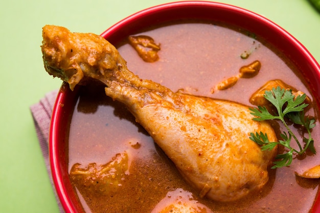 Pikantne czerwonawe curry z kurczaka lub masala, z wyraźnym kawałkiem nogi, podawane w misce lub kadhai na kolorowym lub drewnianym tle. selektywne skupienie.