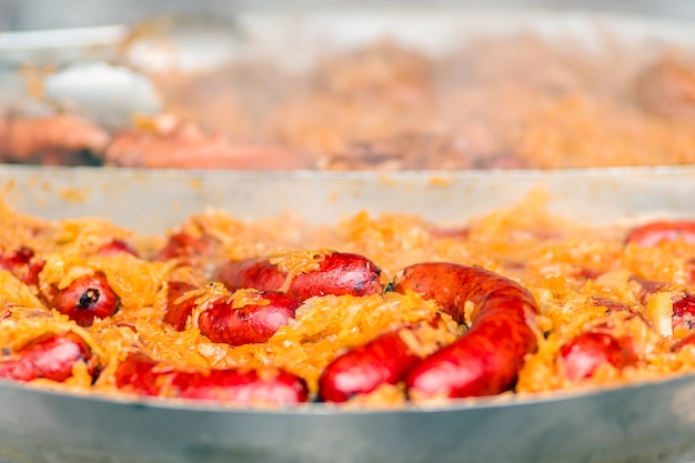 Pikantne czerwone kiełbaski wieprzowe ze złocistą kapustą gotowane na gorącej patelni w miejskiej taryfie