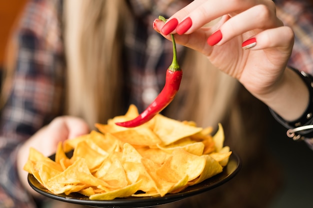 Pikantne frytki na gorąco. ostra ognista przekąska. kobieta ręka trzyma chipsy nacho i czerwona papryka chili