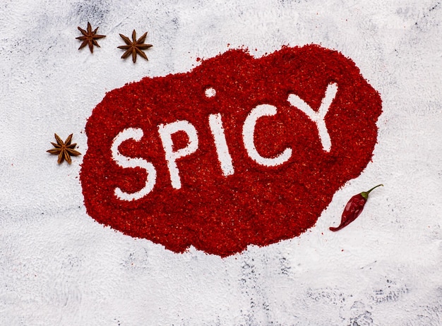 Zdjęcie pikantne słowo napisane na czerwonym proszku chili z strąkiem chili i gwiazdką na białym tle