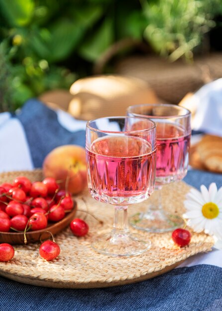 Piknik na świeżym powietrzu na polach lawendy. Wino różowe w kieliszku, wiśnie i słomkowy kapelusz na kocu