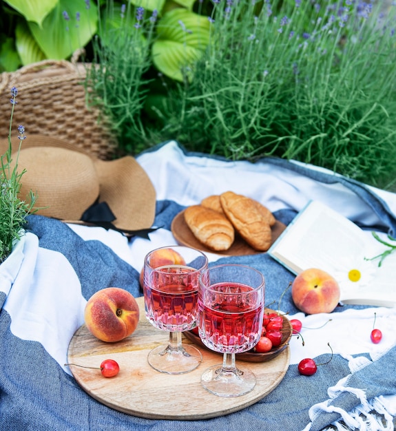 Piknik Na świeżym Powietrzu Na Polach Lawendy. Wino Różowe W Kieliszku, Wiśnie I Słomkowy Kapelusz Na Kocu