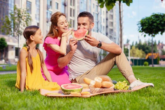 Piknik rodzinny. Radosny zachwycony mężczyzna patrząc na swoją córkę jedząc arbuza