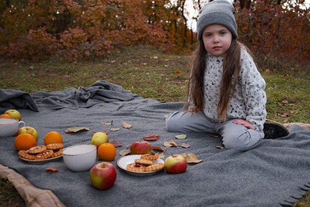 Piknik rodzinny w złotym jesiennym czasie. Matka z dzieckiem dziewczyna pije gorącą czekoladę lub herbatę na zewnątrz w sezonie jesiennym.