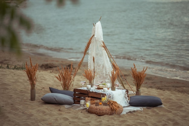 Piknik wieczorem o zachodzie słońca na piaszczystym brzegu morza lub oceanu wystrój w stylu boho i rustykalnym