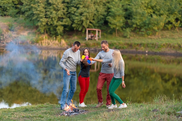 Piknik z przyjaciółmi przy jeziorze w pobliżu ogniska. Firma przyjaciele ma podwyżki natury pyknicznego tło. Turystów relaks w czasie picia. Letni piknik. Zabawa z przyjaciółmi