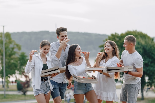 Piknikowi przyjaciele z pizzą i napojami, słoneczny dzień, zachód słońca, towarzystwo, zabawa, pary i mama z dzieckiem