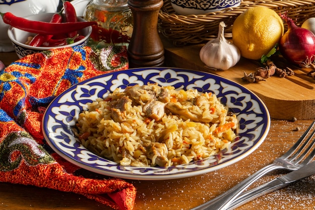 Pilaw z kurczakiem. Tradycyjne orientalne danie na ciepło z gotowanego ryżu, mięsa z kurczaka, warzyw i przypraw w talerzu z narodowym ornamentem uzbeckim.