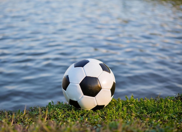Piłka nożna siedzi na trawie nad wodą.