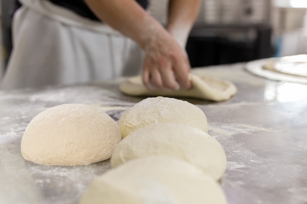 Piłka pizzy ciasto na stole z rękami szefa kuchni zagnieść ciasto w tle.