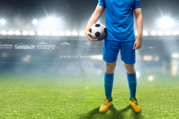 Piłkarz w niebieskiej koszulce stoi i trzyma piłkę