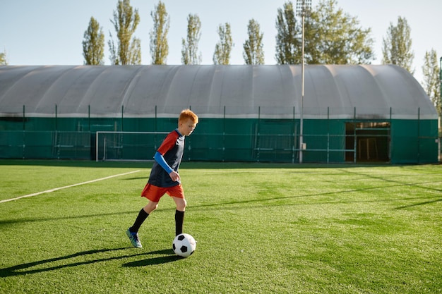 Zdjęcie piłkarz w wieku podstawowym kopie piłkę trenującą na boisku piłkarskim