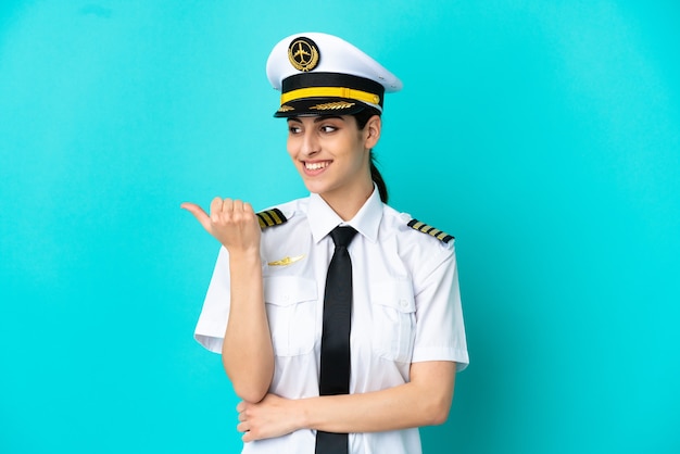 Pilot samolotu kaukaska kobieta na białym tle na niebieskim tle wskazująca na bok, aby zaprezentować produkt
