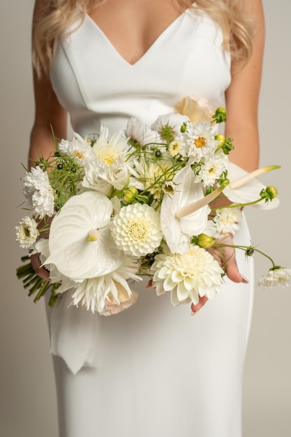 Pionowe, nierozpoznawalne, przycięte, stylowe, modne kobiece ciało w białej sukni z niskim dekoltem, trzymające elegancki bukiet kwiatów