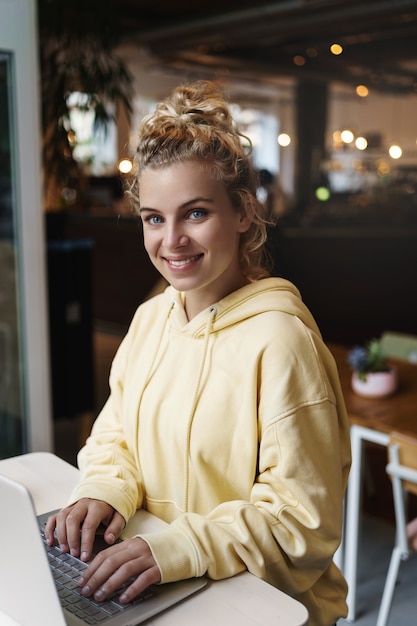 Pionowe strzał uśmiechnięta atrakcyjna dziewczyna pracująca z laptopem w kawiarni.