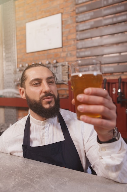 Zdjęcie pionowe ujęcie profesjonalnego barmana badającego jasne piwo w szkle