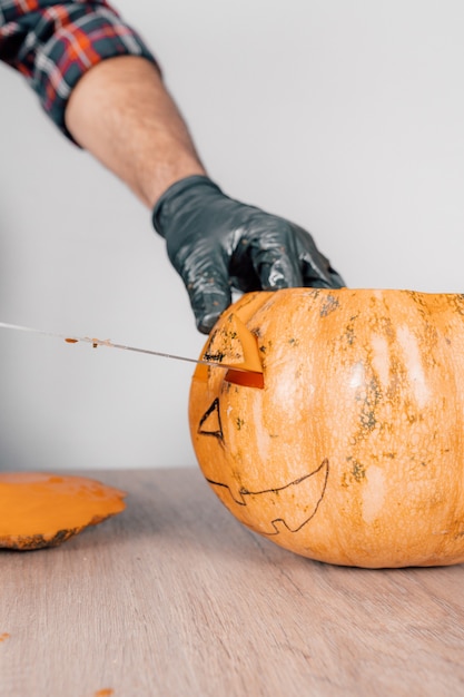 Zdjęcie pionowe ujęcie przedstawiające osobę w rękawiczkach i rzeźbiącą dynię na halloween