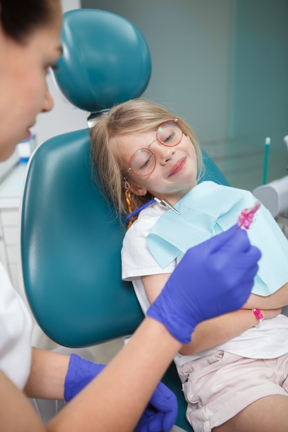 Pionowe ujęcie słodkiej szczęśliwej dziewczyny na wizycie u dentysty w klinice