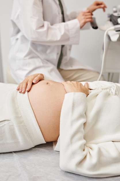Pionowe zbliżenie młodej kobiety w ciąży przygotowującej się do USG w klinice medycznej z naciskiem na brzuch