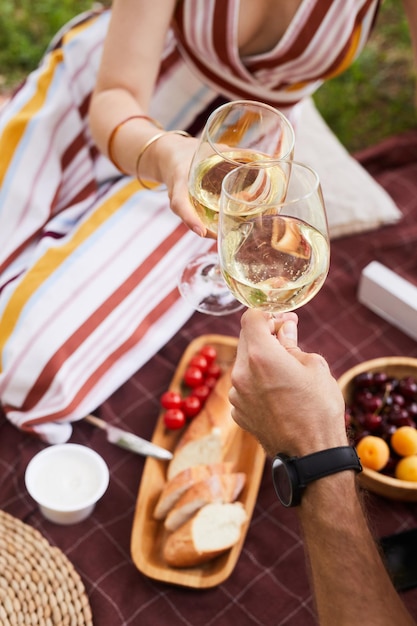 Pionowe zbliżenie młodej pary trzymającej kieliszki do wina podczas romantycznego pikniku na świeżym powietrzu.