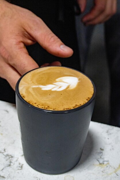 Pionowe zbliżenie ręki biorącej kubek waniliowej latte