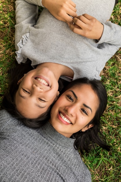Pionowe zdjęcia młodej matki Łacińskiej i jej córki leżącej na trawie.