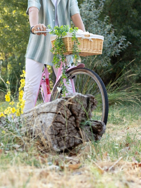 Pionowo przycięty widok nierozpoznawalnego młodego mężczyzny na różowym rowerze vintage z koszem i roślinami