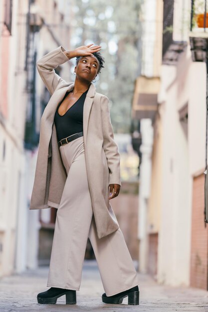 Zdjęcie pionowy portret afrykańskiej modelki w płaszczu pozującej stojąc na ulicy