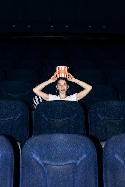 Zdjęcie pionowy portret kobiety siedzącej na krześle w kinie jedzącej w ręku miskę z popcornem