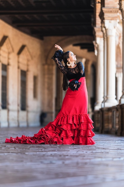 Pionowy portret kobiety w czerwonej sukience flamenco tańczącej na zewnątrz starożytnego budynku