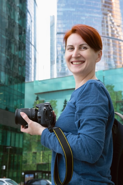 Zdjęcie pionowy portret kobiety z aparatem miejski fotograf fotografuje nowoczesną architekturę kobieta uśmiecha się i patrzy w kamerę