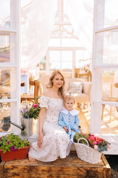 Pionowy portret ładnej blond młodej matki w sukience siedzącej na progu letniej gazebo