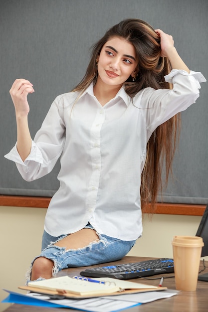Pionowy portret młodej dziewczyny siedzącej w biurze i rozciągającej włosy