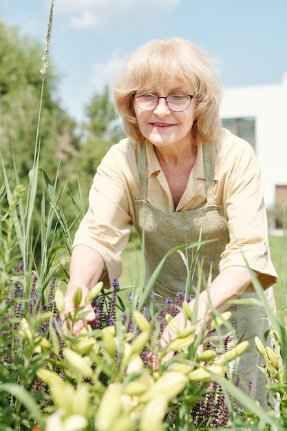 Pionowy portret pięknej starszej kobiety w okularach, cieszącej się pracą w jej przydomowym ogrodzie