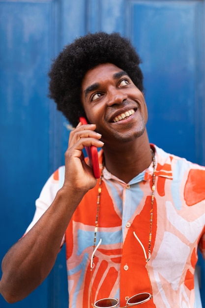 Pionowy portret szczęśliwy czarny człowiek rozmawia przez telefon African American man z fryzurą afro za pomocą telefonu komórkowego na ulicy Koncepcja życia i technologii