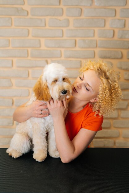 Pionowy portret szczęśliwy żeński groomer trzymający kędzierzawy pies Labradoodle po strzyżeniu w salonie fryzjerskim Atrakcyjna kobieta domowych fryzjer robi profesjonalną opiekę w weterynaryjnej klinice spa