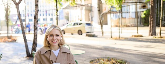 Zdjęcie pionowy portret uśmiechniętej blondynki, studentki z kawą i laptopem, ma notatniki