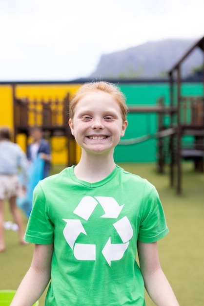 Pionowy portret uśmiechniętej kaukaskiej dziewczyny noszącej recyklingową koszulkę na dziedzińcu szkolnym z miejscem do kopiowania