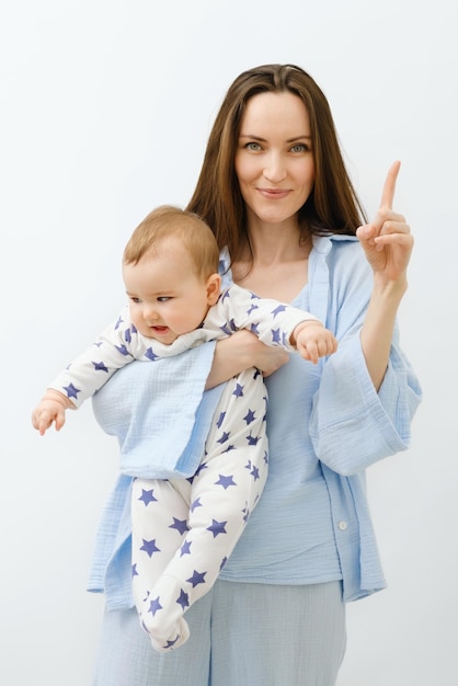 Pionowy portret uśmiechniętej matki z dzieckiem w dłoniach stojącej na białym tle matka w niebieskich ubraniach wskazująca palcem w górę na reklamę