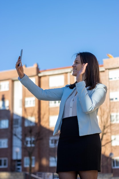 Pionowy portret uśmiechniętej młodej bizneswoman kaukaskiej podczas rozmowy wideo na ulicy