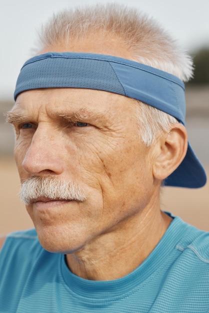 Pionowy portret z bliska białego starszego mężczyzny w niebieskiej czapce sunvisor patrzącego w inną stronę