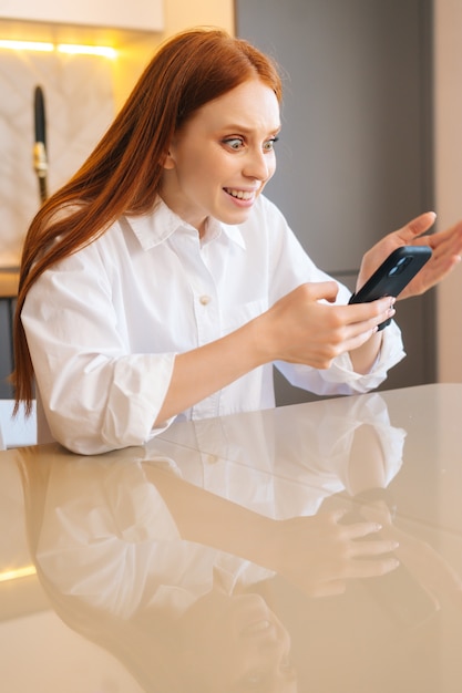 Zdjęcie pionowy portret zdziwionej, zszokowanej młodej kobiety, mówiącej „wow, używając telefonu, miej niespodziankę lub