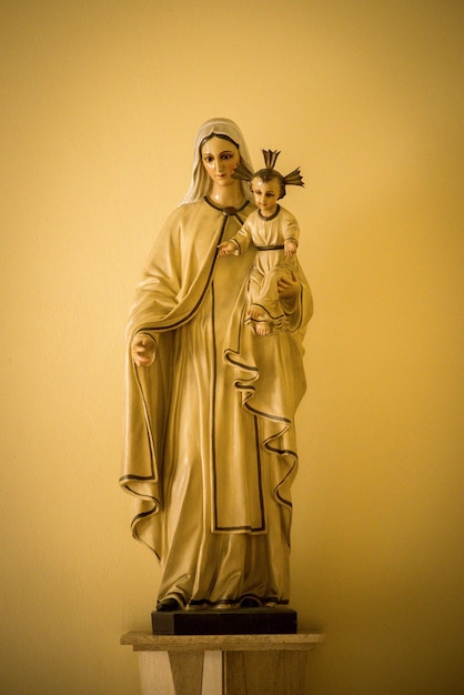 Zdjęcie pionowy ujęcie posągu maryi matki jezusa trzymającego jezusa chrystusa z żółtą ścianą za nim.