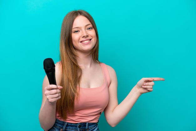 Piosenkarka kaukaska kobieta podnosi mikrofon odizolowany na niebieskim tle wskazując palcem na bok
