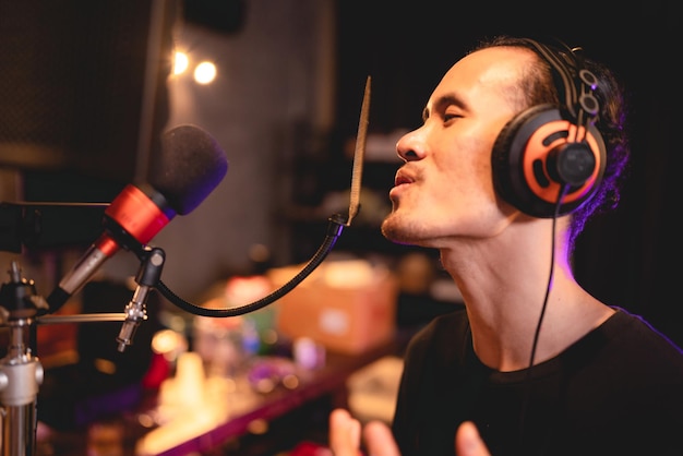 Piosenkarka nosząca słuchawki pracująca nad nagrywaniem i wykonaniem głosu muzycznego z profesjonalnym mikrofonem w studiu audio Wokalista śpiewa piosenkę z muzykiem artystą i inżynierem dźwięku prowadzącym transmisję na żywo