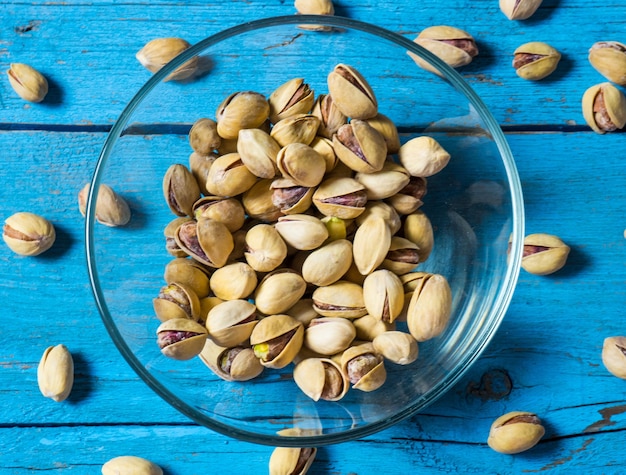 Pistacje w przezroczystej szklanej misce na starym drewnianym stole, klimatyczna rustykalna kompozycja, kopia przestrzeń