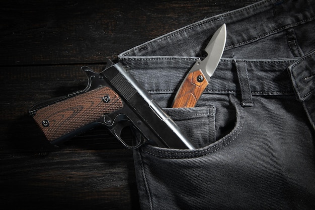 Pistolet i nóż na kieszeni dżinsów na ciemnym tle